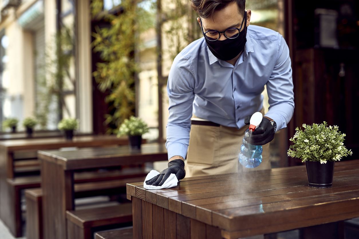 Employee disinfecting table with mask on
